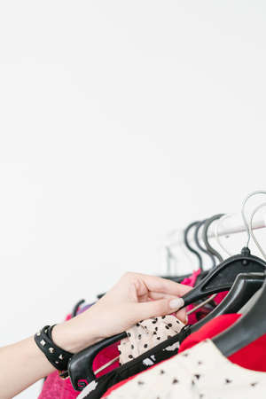 fashion and clothing. personal style and popular trends. self expression and creativity. woman hand choosing outfit from bright clothes hanging on the rack. white background with copyspace.の写真素材