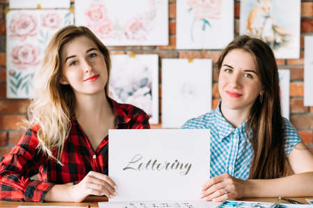 art school lettering classes. creative handwriting courses. brush calligraphy learning. student and teacher holding paper with text.の写真素材