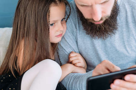 family problems lack of communication and digital device addiction. child daughter hugging her daddy. father looking at mobile phone. bad parenting habits and irresponsible fatherhood.の写真素材