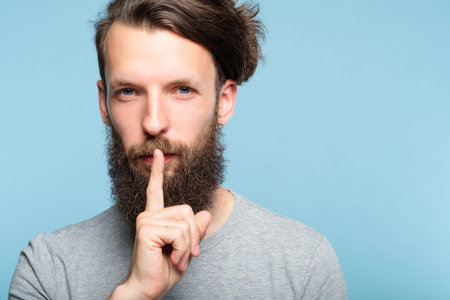 shh silence and quiet concept. man showing finger on lips gesture. portrait of a bearded hipster guy...
