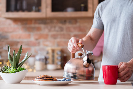 traditional quick breakfast of tea and pastry. food and eating habits concept. man holding kettle...