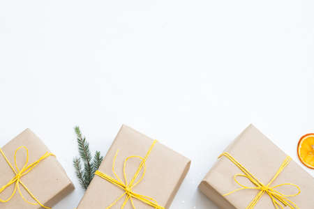 holiday season and christmas background. three presents in craft paper packaging tied with yellow twine on white backdrop. fir tree twig and dried citrus decor elements. free space conceptの写真素材