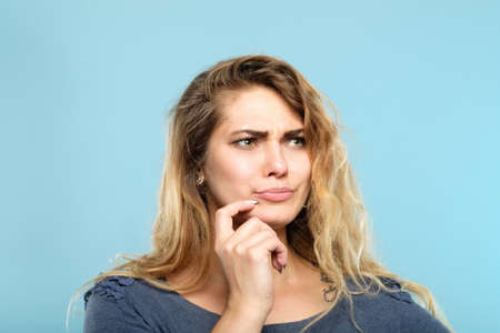 facial expression. quizzical grumpy thoughtful woman. young beautiful girl portrait on blue background.の写真素材