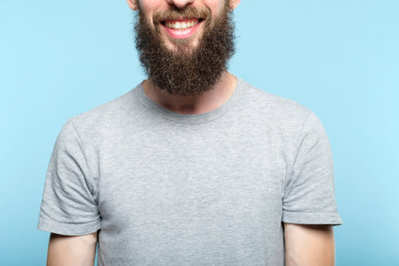 man joyful happy smile. cropped portrait of a young bearded guy on blue background. emotion facial...