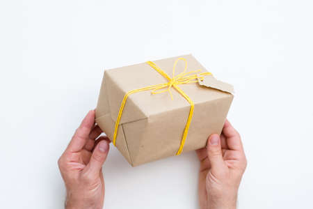 handcrafted present. heartfelt congratulation and reward for a special person. hands holding gift wrapped in paper and tied with yellow twine. festive package on white background.の写真素材