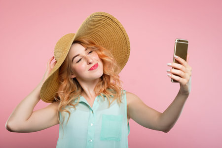 selfie and self adoration. young stylish woman in a big sunhat taking a photo of herself using...