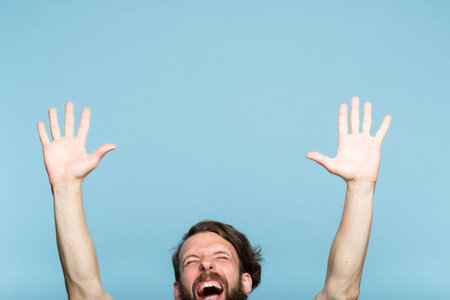 happiness enjoyment and laugh. excited man with hands in the air. portrait of a young bearded guy on blue background. emotion facial expression. feelings and people reaction.の写真素材