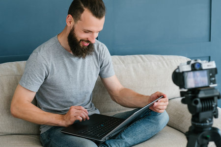 content creation for social media. bearded man holding laptop and shooting video of himself using...