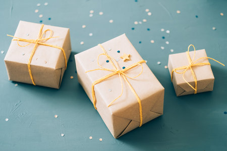 handmade presents. three gift boxes packaged in craft paper and tied with yellow twine on blue...