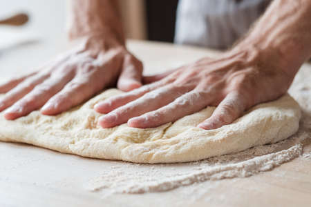 food and pastry concept. preparing and cooking skills concept. man hands flattening dough.の写真素材