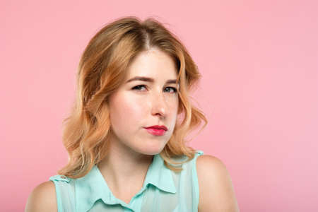emotion expression. suspicious thoughtful dubious woman with a distrustful look. young beautiful blond girl portrait on pink background.の写真素材