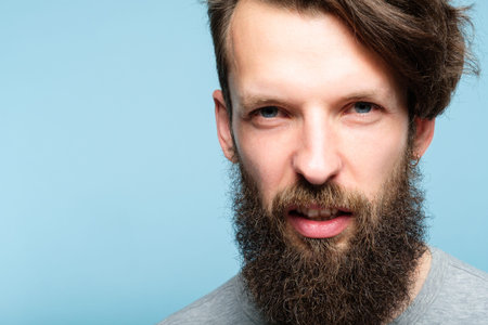man with a scornful disdainful disrespectful look. portrait of a young bearded guy on blue...
