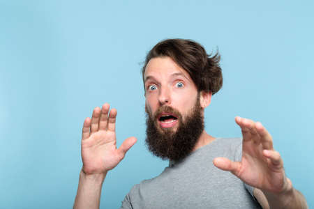 surprised startled shocked man. gasping of fright. portrait of a taken aback bearded guy on blue background. emotion facial expression. people reaction concept.の写真素材