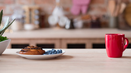 healthy eating and morning food. quick and easy breakfast. pastry poppy seed bun and fresh blueberry. tea or coffee in a red mug on a kitchen table.の写真素材