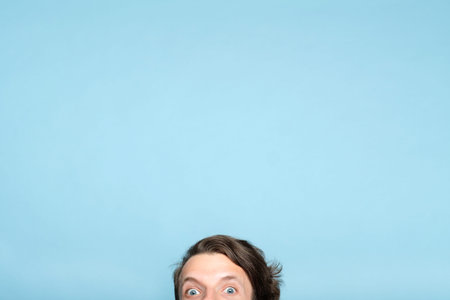startled eccentric whimsical man with smiling eyes peeping out from the bottom of blue background....