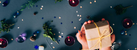 festive new year holiday decor. hands holding craft gift box. seasonal adornments and candles on blue background for landing page.の写真素材