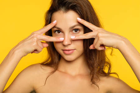 cute and pretty young woman gesturing the V sign. brown haired girl portrait on yellow background. fun amusement and disco concept.の写真素材