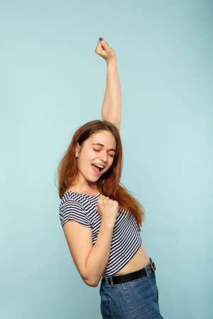 winning success and achievement. happy joyful smiling girl making a victory gesture her hand in the air. excited thrilled woman portrait on blue background.の写真素材