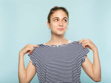 shopping fashion and clothes fitting. smiling young beautiful girl trying on a stripy shirt. blue backgroundの写真素材