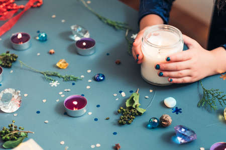 festive christmas decoration. hands holding candle. seasonal adornments on blue background.の写真素材