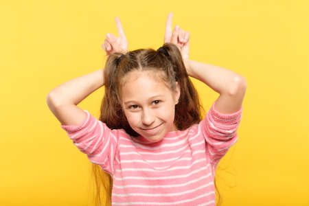 girl making horns with her hands. mischievous childish behavior and naughtiness.の写真素材