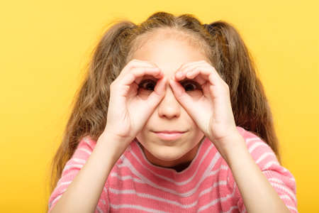 girl pretending to look through binoculars made of hands. search concept.の写真素材