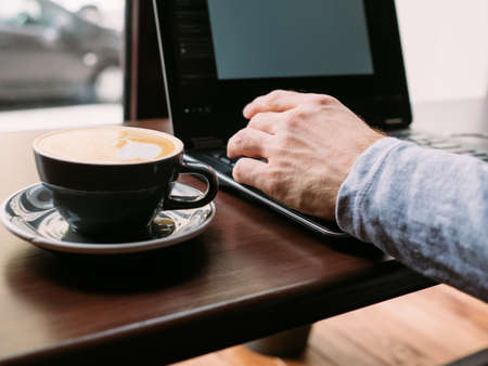 coffee break and work. man hands typing on laptop. cup of cappuccino on the table.の写真素材