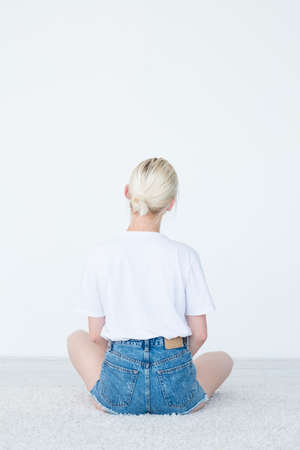 backview of a woman sitting on the floor looking at invisible object on white background.
