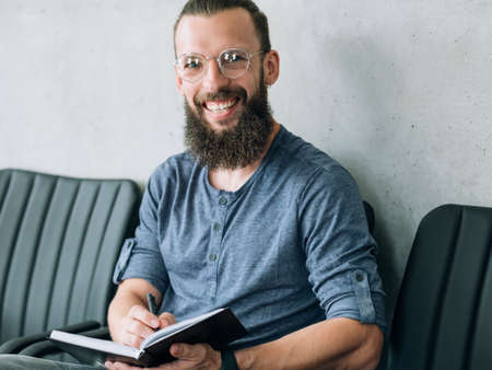 smiling bearded man in glasses with notepad in his hands. student education or training courses concept.の写真素材
