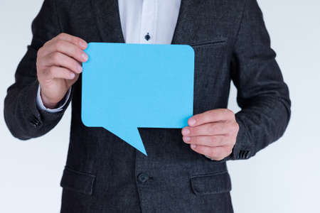 man holding blue paper in shape of empty speech bubble. icon of social media communication and ideas.の写真素材