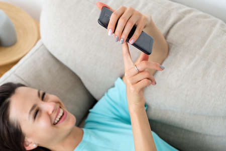 laughing woman laying on the couch using phone. idle lifestyle and mobile devices addiction.の写真素材