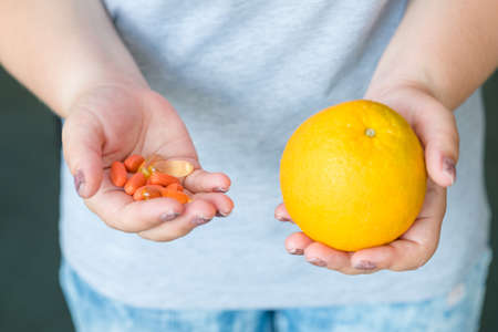 pill supplemens vs natural vitamins choice. drugs and citrus in woman hands.の写真素材