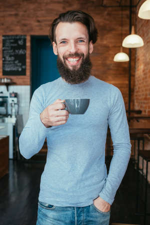 smiling happy man standing in coffee shop holding cup of hot drink. caffeine energy boostの写真素材