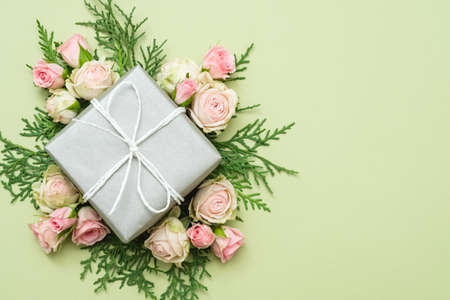 present gift box in silver paper and bunch of roses and twigs composition on light green background.の写真素材