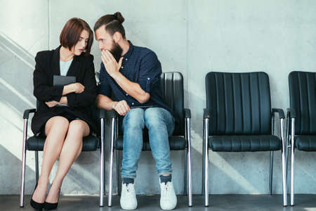 man whispering to a womans ear. office gossip and secrets. colleagues in business workspace.の写真素材