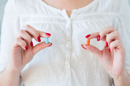 woman in white holding red and blue pills. medication treatment and healthの写真素材
