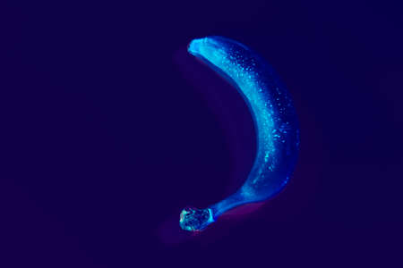 Conceptual neon art. Vibrant glow banana on dark purple background.の写真素材