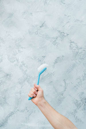 Cleaning concept. Raised hand holding blue brush. Copy space on grey textured background.