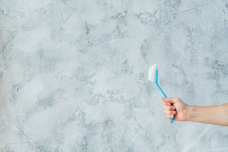 Home cleanup strategy. Hand holding brush. Copy space on grey textured background.の写真素材