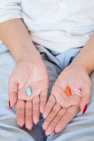 Drug incompatibility. Choice concept. Woman holding red and blue pill in handsの写真素材