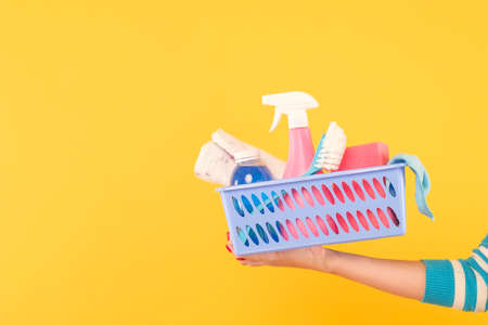Home cleaning products. Housekeeping concept. Hand holding a basket with supplies. Copy space on yellow background.の写真素材