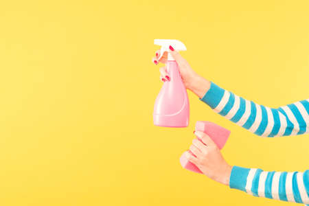 Home cleaning concept. Cleanup services. Hands holding atomizer and sponge. Copy space on yellow background.の写真素材