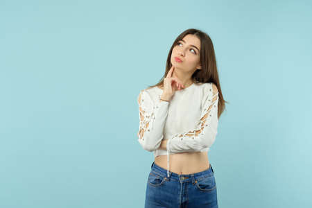 Thoughtful pensive young woman touching neck and looking at virtual object. Copy space on blue background.の写真素材
