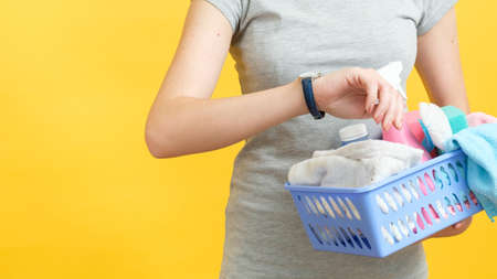 Quick cleaning. Organized wife time management. Woman torso with basket of supplies looking at watch. Copy space on yellow background.の写真素材