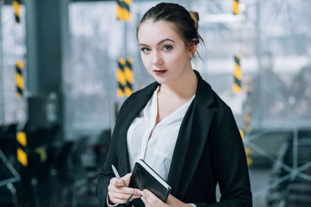 Business employee portrait. Thoughtful young woman with notebook standing in office workspace.