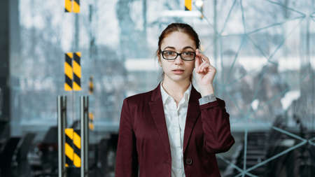 Workaholic intern. Empty office workspace. Young woman with hand at glasses looking directly at camera.の写真素材