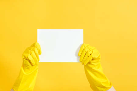 Home cleaning to do list. Hands in rubber gloves holding blank paper mockup. Copy space on yellow...