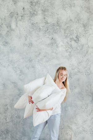 Feather pillows. Housewife choice. Smiling young woman holding comforting pile. Copy space on grey background.の写真素材
