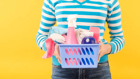 House cleanup. Basic cleaning set. Woman holding basket of supplies. Copy space on yellow background.の写真素材