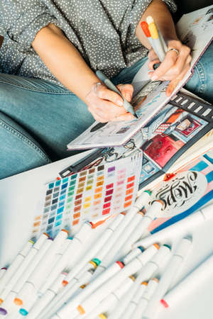 Artist sketching. Workplace. Woman painter drawing in sketchbook with palette and supplies around.の写真素材